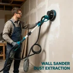Worker using drywall sander with dust extraction on vertical wall – tool connected to vacuum hose, no visible dust cloud during sanding.